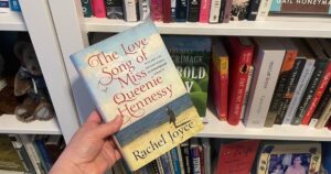 The Love Song of Miss Queenie Hennessy being held by bookshelf