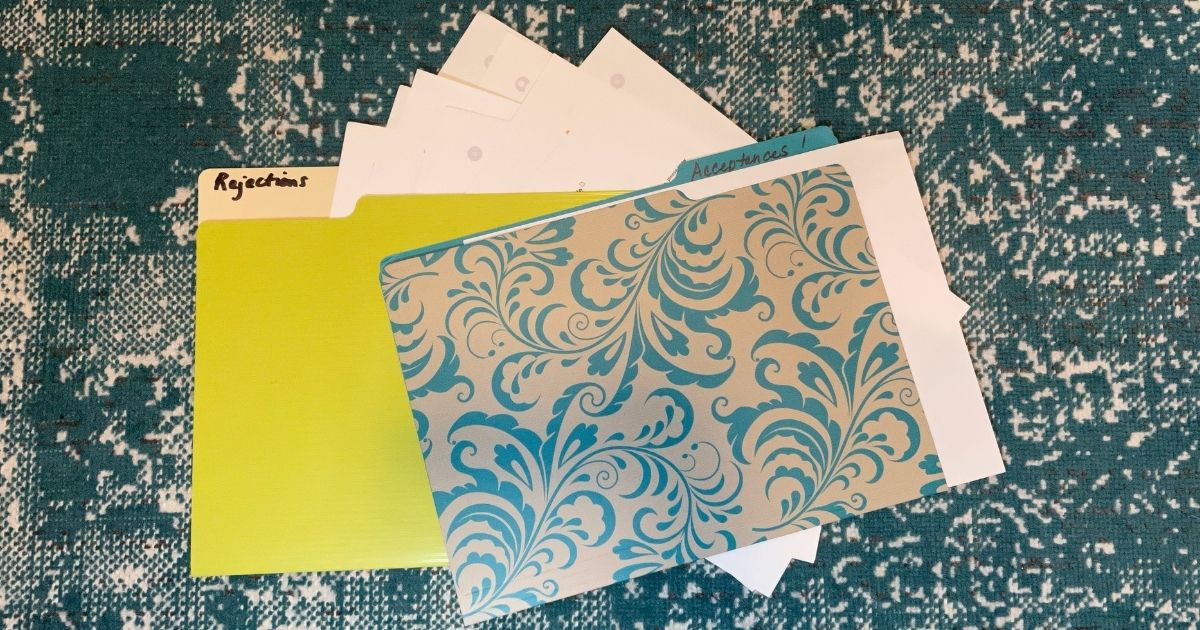 two file folders, a green one and a turquoise and gray floral one labeled Rejections and Acceptances! Several sheets of paper visible sticking out from folders.