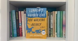 a yellow and blue book titled London's Number One Dog Walking Agency: A Memoir by Kate MAcDougall sits on a white bookshelf surrounded by other memoirs