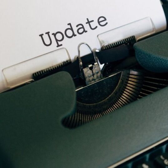 A dark green manual typewriter with a piece of typing paper in the carriage and the words Update typed in large letters on the page